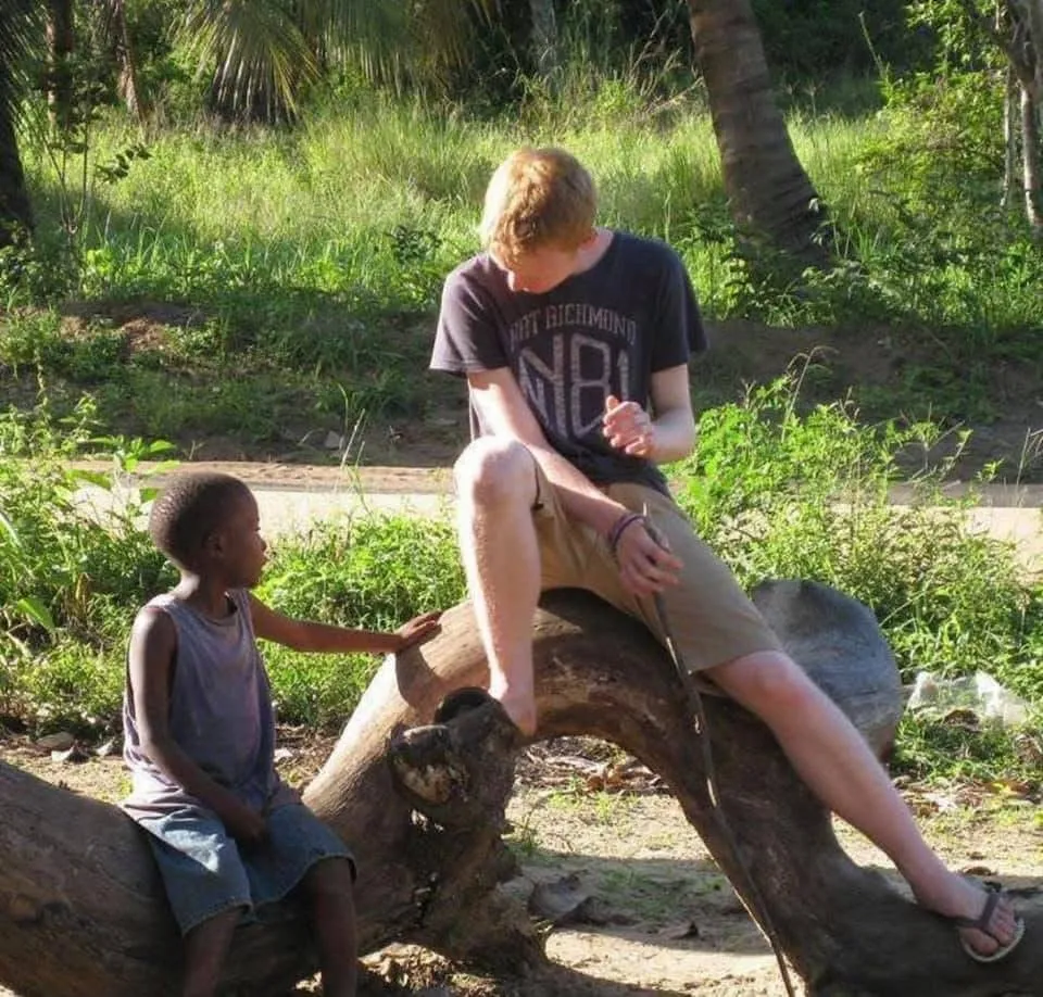 Me sitting on a fallen tree in Kenya, next to a young boy